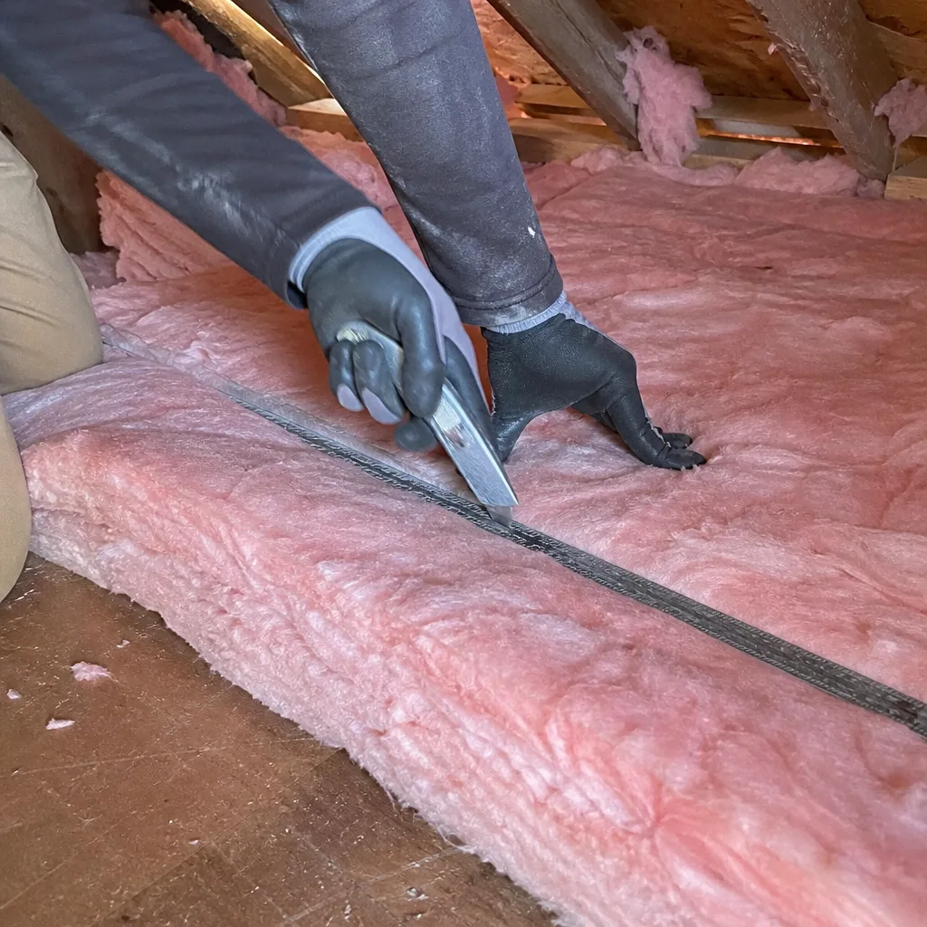 Worker cutting fiberglass insulation batting for attic installation
